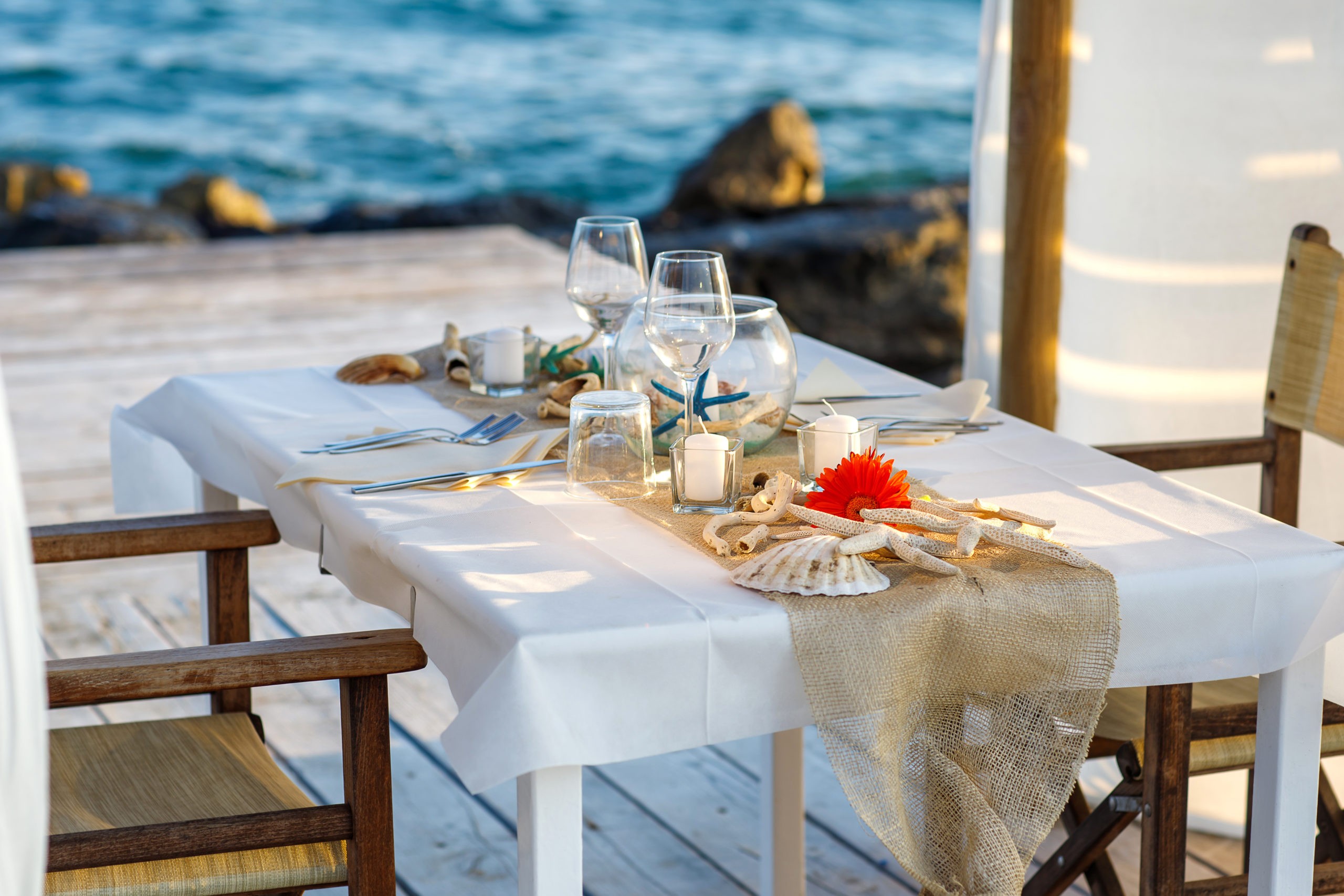 Dinner table set for two in a beach style next to rocks with waves crashing