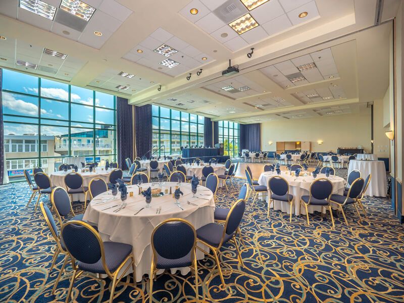 Large room with blue and gold carpet with windows from the floor to the ceiling with a tables set up in it