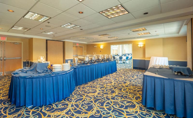 Room with blue and gold patterned carpet and tables with blue table cloth set up for catering