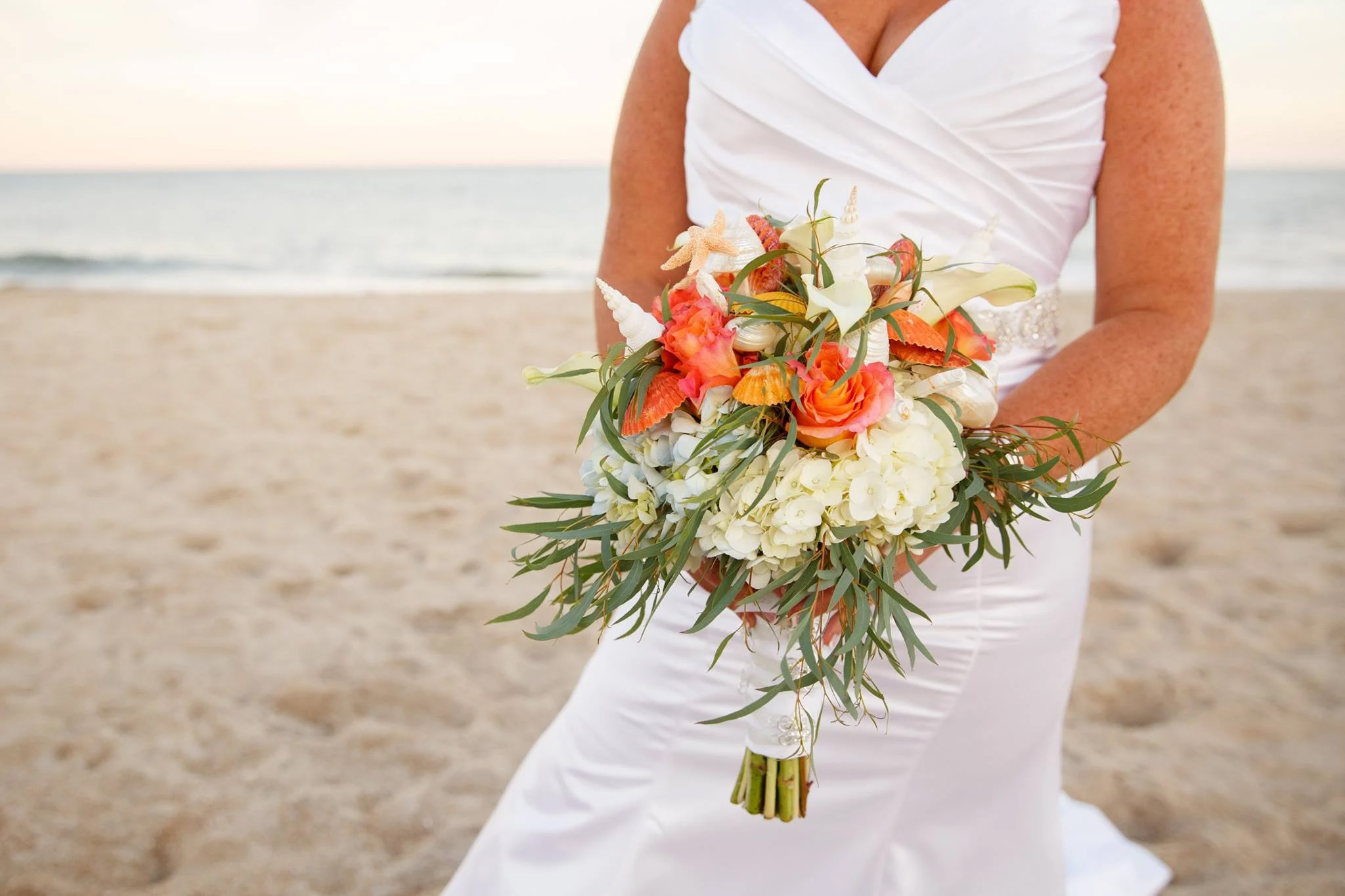 Bride holding bouquet on beach at sunset