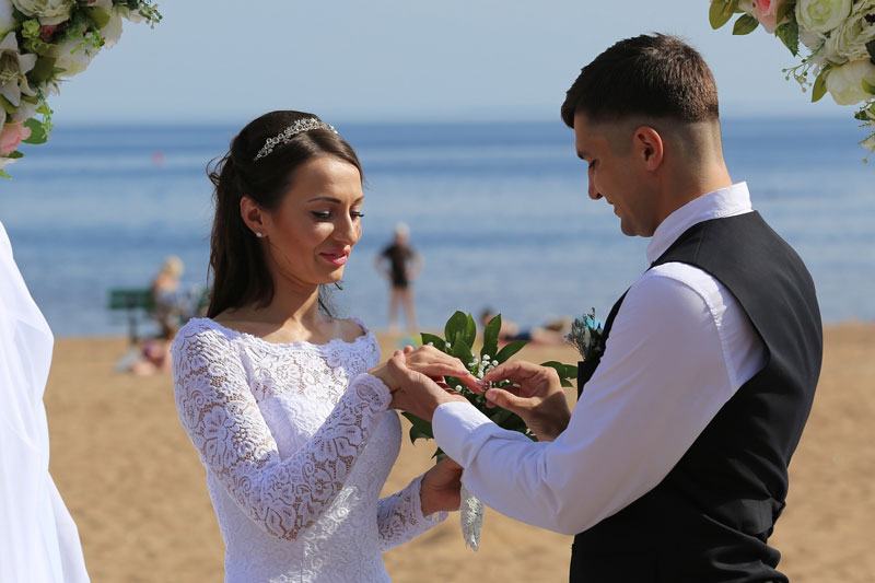 Groom putting ring on brides finger on the beach