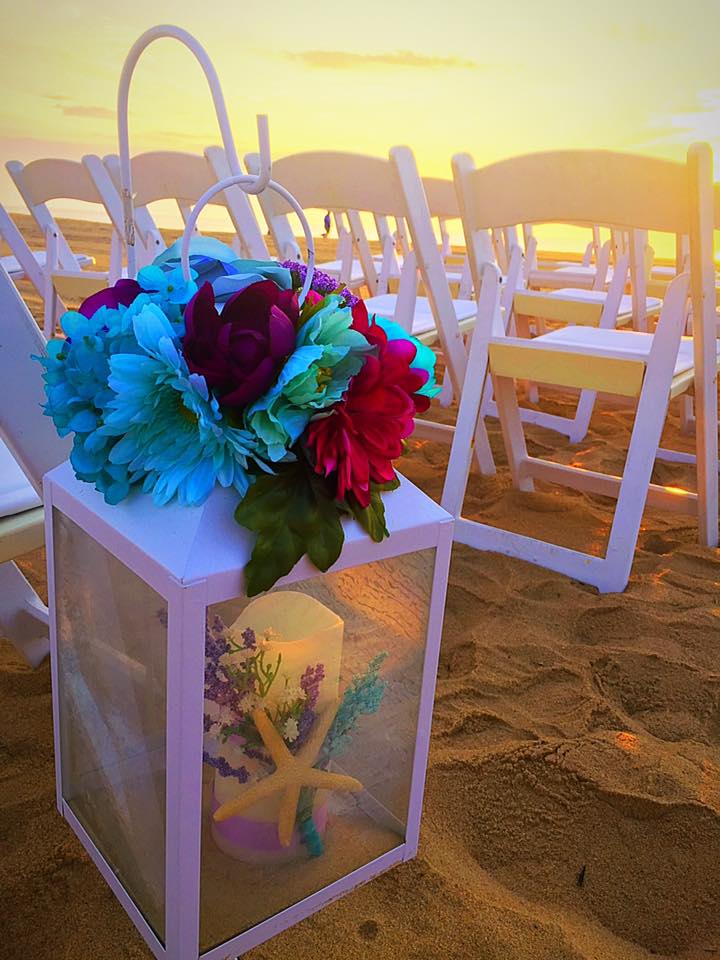 lantern with floral decorations and a candle inside on the sand in a row with White folding chairs